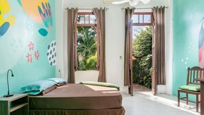 A room with a bed, a desk, and a chair. There are two windows with curtains, and a view of greenery outside. - casaJOMO (Rio de Janeiro)