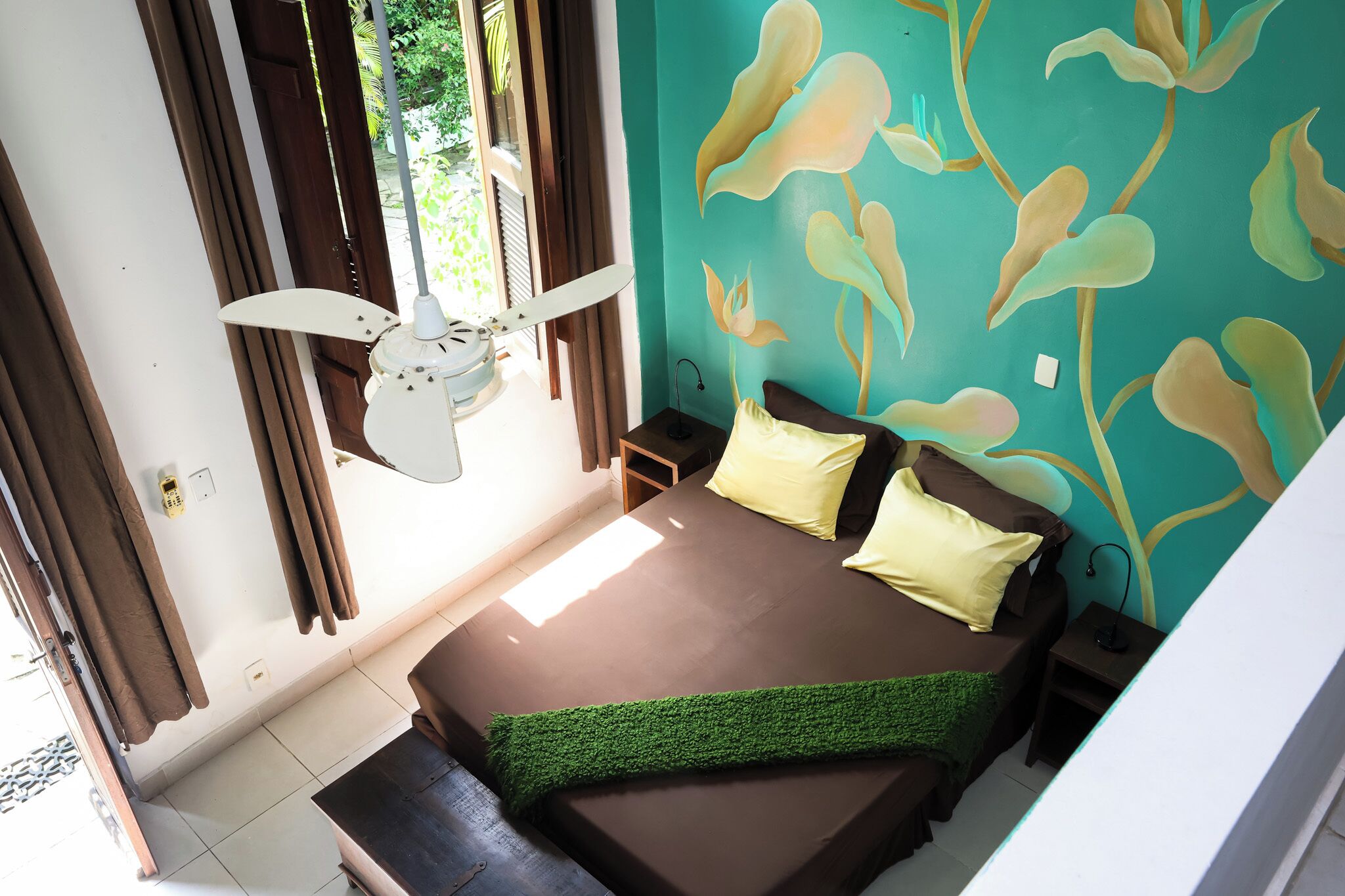 A bedroom with a bed, curtains, a ceiling fan, and a wall with a floral pattern.