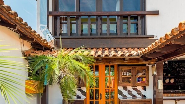 A building with a tiled roof, a wooden door, and a small outdoor seating area with a white planter and palm tree. - casaJOMO (Rio de Janeiro)