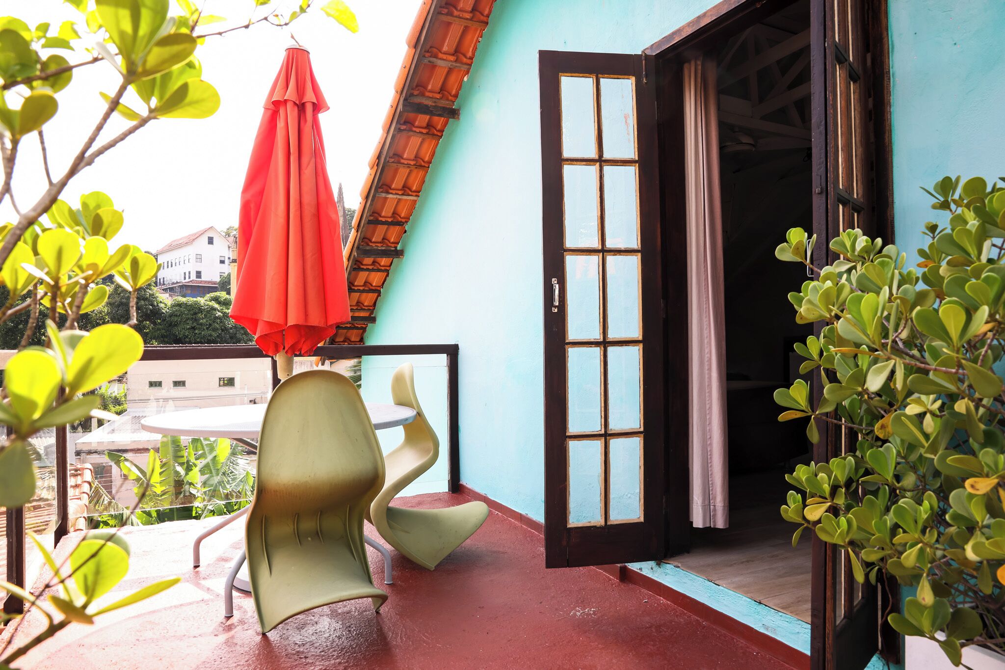 Puerta abierta que da a una habitación con vistas a un edificio al fondo, un paraguas rojo y una silla verde en el exterior.