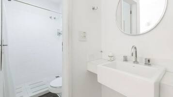 A bathroom with a white toilet, a shower with a glass door, a sink with a mirror, and a bottle of hand soap.