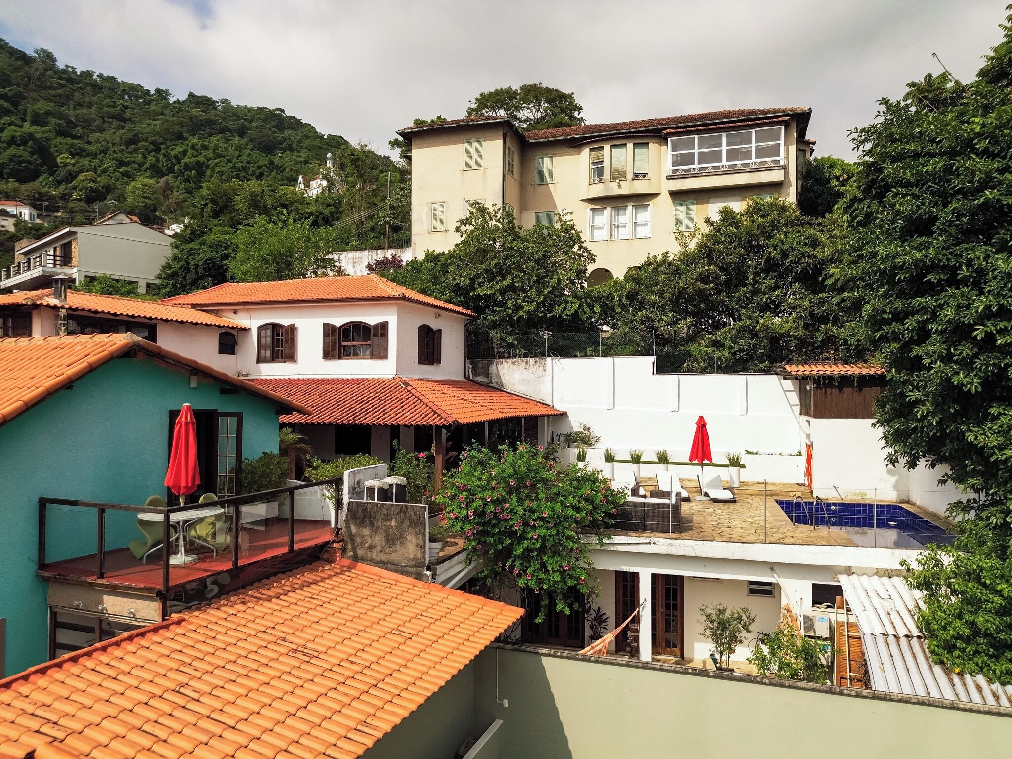 Zona residencial com vários edifícios, uma piscina e uma varanda com um guarda-sol vermelho.