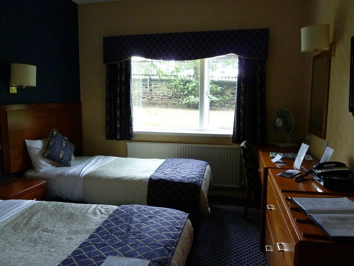 Ein Hotelzimmer mit zwei Betten, einem Schreibtisch mit Telefon und einem Fenster mit Vorhängen.