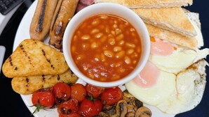 Un plato de comida para el desayuno con salchichas, tostadas, frijoles, huevos, champiñones y tomates.