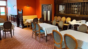 Un restaurante con varias mesas y sillas, una alfombra estampada y una pared roja.
