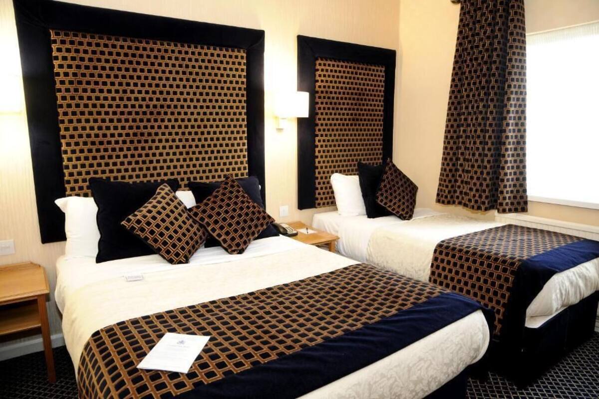 A hotel room with two beds, each with a patterned bedspread and pillows, a nightstand, and a window with curtains.