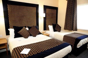 A hotel room with two beds, each with a patterned bedspread and pillows, a nightstand, and a window with curtains.