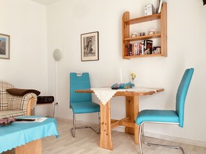 Un salon chaleureux avec une table en bois, deux chaises bleues, une bibliothèque et un tableau encadré au mur.