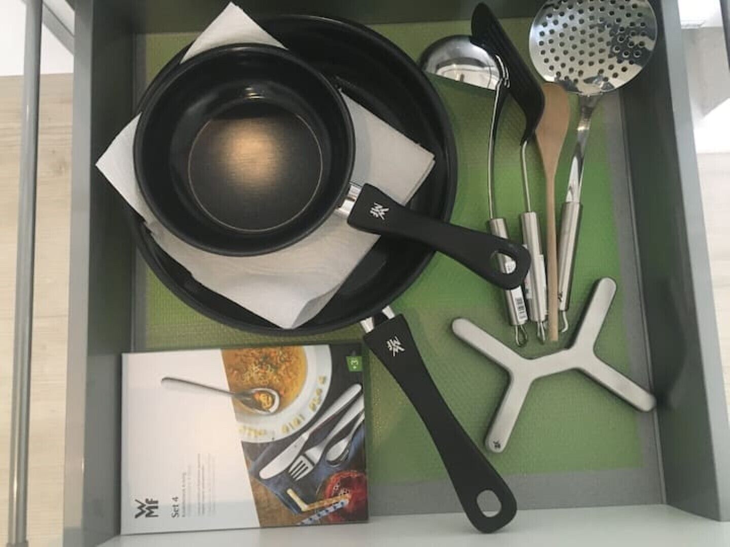 Un tiroir de cuisine contenant une poêle, une spatule, une louche et un livre de recettes.