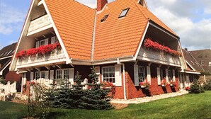 Ein zweistöckiges Haus mit einem steilen Dach, einem Balkon mit roten Blumen und einem gepflegten Rasen.