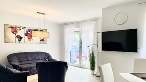 Ein modernes Wohnzimmer mit einer Couch, Sesseln, einem Esstisch und einem Flachbildfernseher.