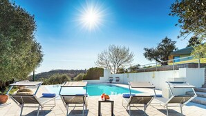 Un área junto a la piscina con sillones reclinables, una mesa con frutero y vista despejada al agua.