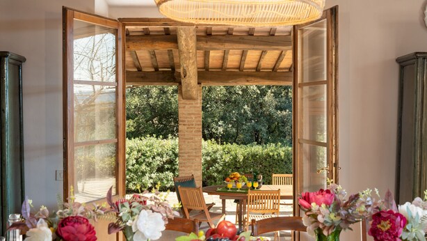 Une structure ouverte en bois, avec une table dressée pour le petit-déjeuner, entourée de chaises, et une vue sur un jardin à la végétation luxuriante.