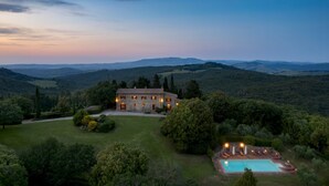 Une maison en pierre avec une piscine, entourée d’une végétation luxuriante et avec des collines en arrière-plan.