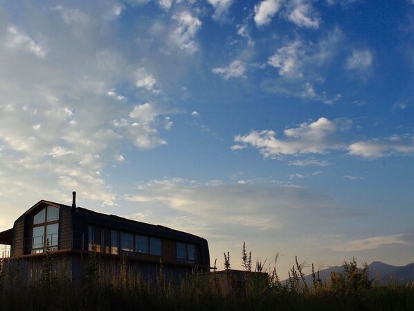 A modern building with large windows and a flat roof, surrounded by tall grasses and mountains in the background. - Shimazaki Toson Yukari no Yado Nakadanaso (Komoro)