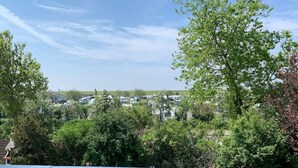 A view from a balcony overlooking a parking area with trees and a clear sky. - Apartment with a view of the dyke for up to 4 people. -Turquoise (Büsum)