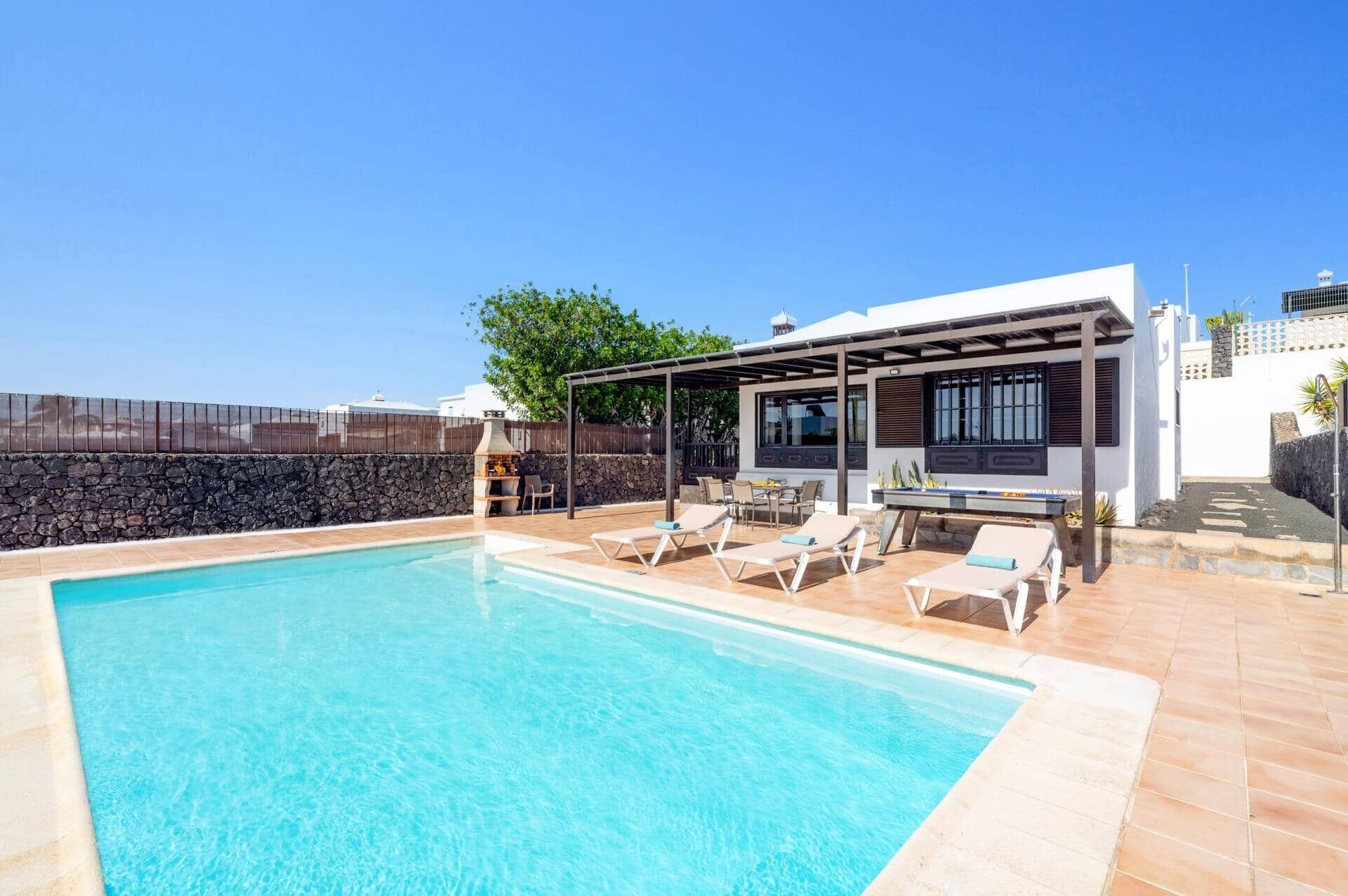 Une piscine avec des chaises longues, un espace barbecue et un patio couvert.