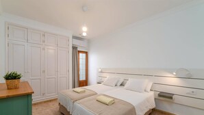 Ein Schlafzimmer mit zwei Betten, einem Kleiderschrank, einem Nachttisch und einer kleinen Pflanze.