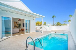 Una piscina en la azotea con vistas despejadas a palmeras y un edificio blanco con puertas correderas de vidrio.