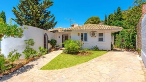 A small white house with a tiled roof, a stone pathway leading to the entrance, and a well-maintained garden. - Villa Mi Sueno by Villa Plus (La Capellania)