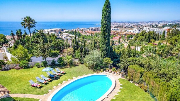 A swimming pool surrounded by a well-maintained lawn, with a view of the sea and a cityscape in the background. - Villa Mi Sueno by Villa Plus (La Capellania)
