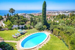 A swimming pool surrounded by a well-maintained lawn, with a view of the sea and a cityscape in the background. - Villa Mi Sueno by Villa Plus (La Capellania)