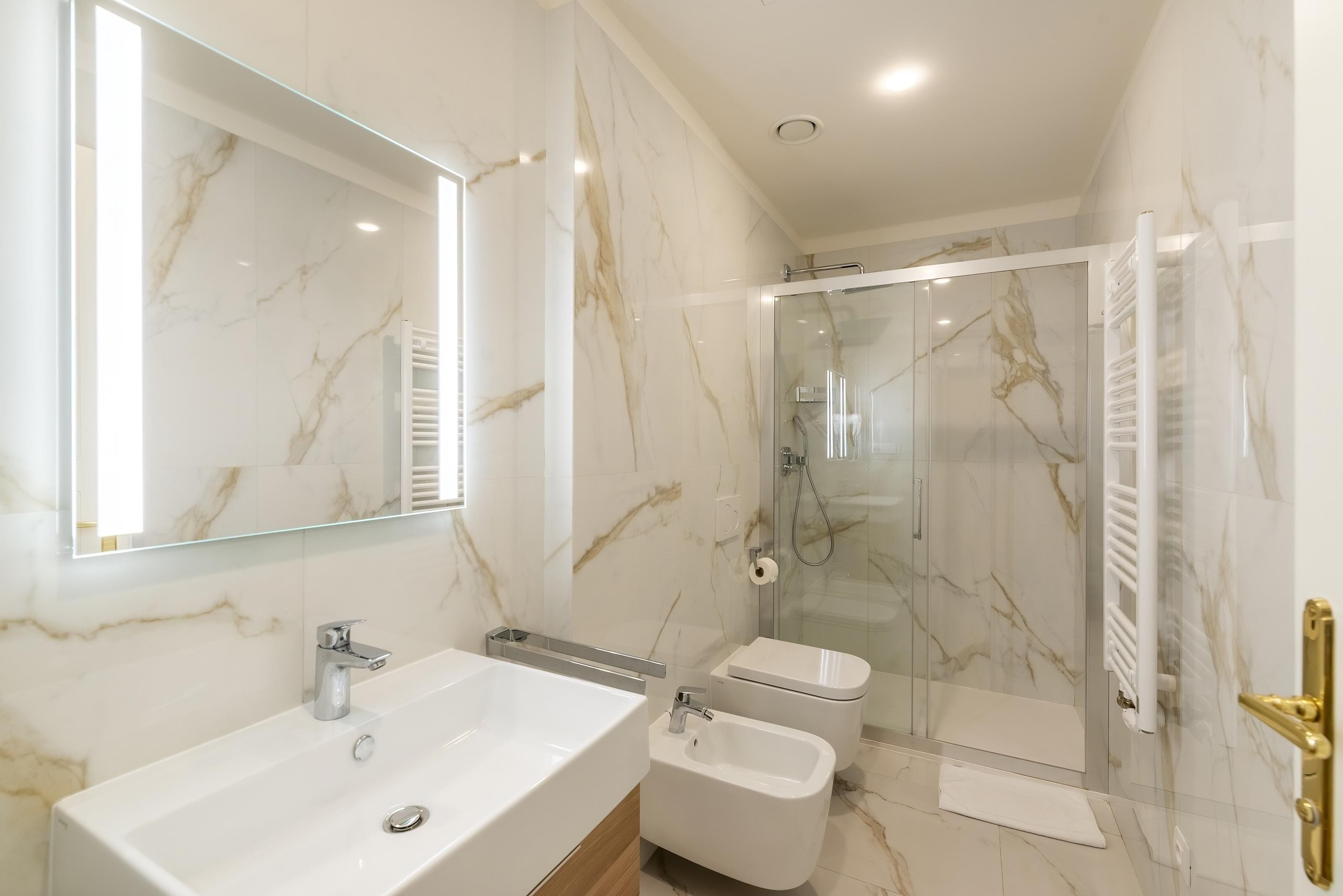 A modern bathroom with a marble sink, a glass-enclosed shower, and a toilet.
