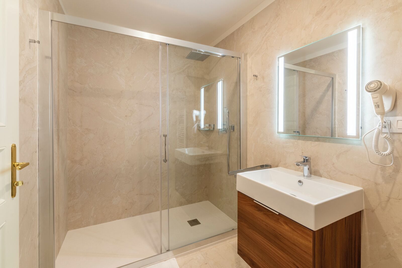 A modern bathroom with a glass-enclosed shower, a vanity with a sink, and a hairdryer mounted on the wall.