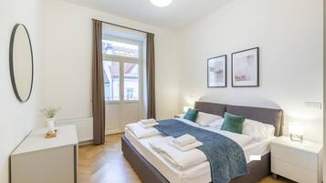 A modern bedroom with a large bed, bedside tables, a window with curtains, and framed pictures on the wall.