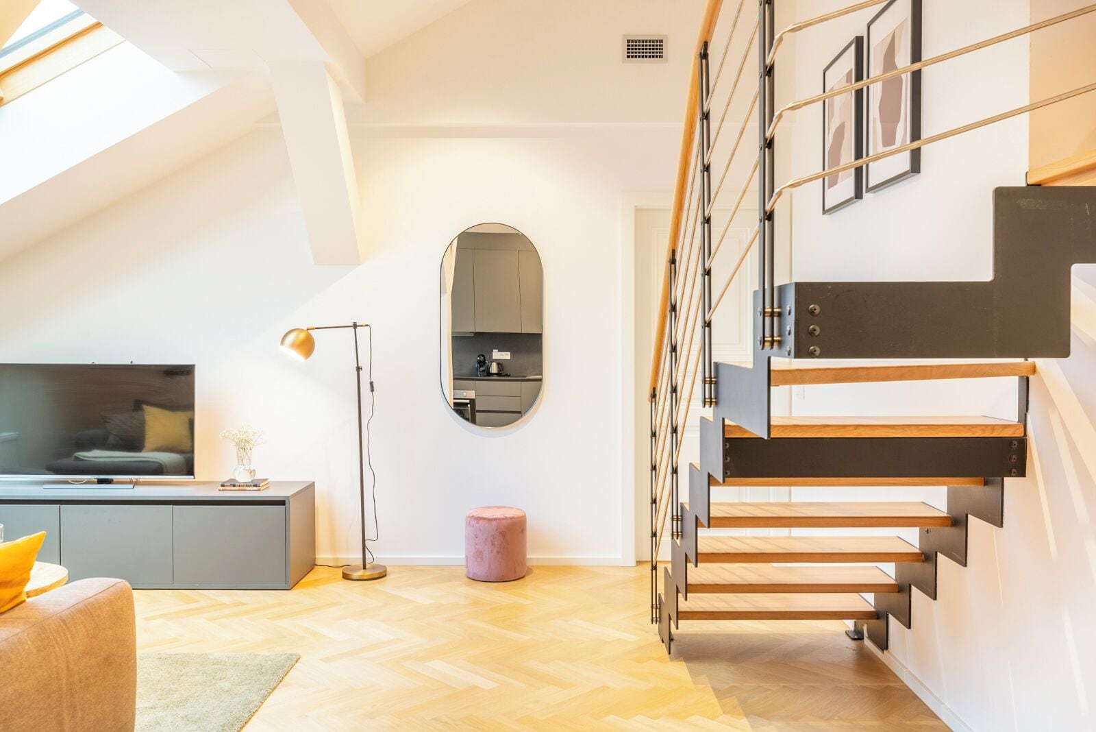 Een moderne woonkamer met een trap, een televisie, een vloerlamp en een rond poef.