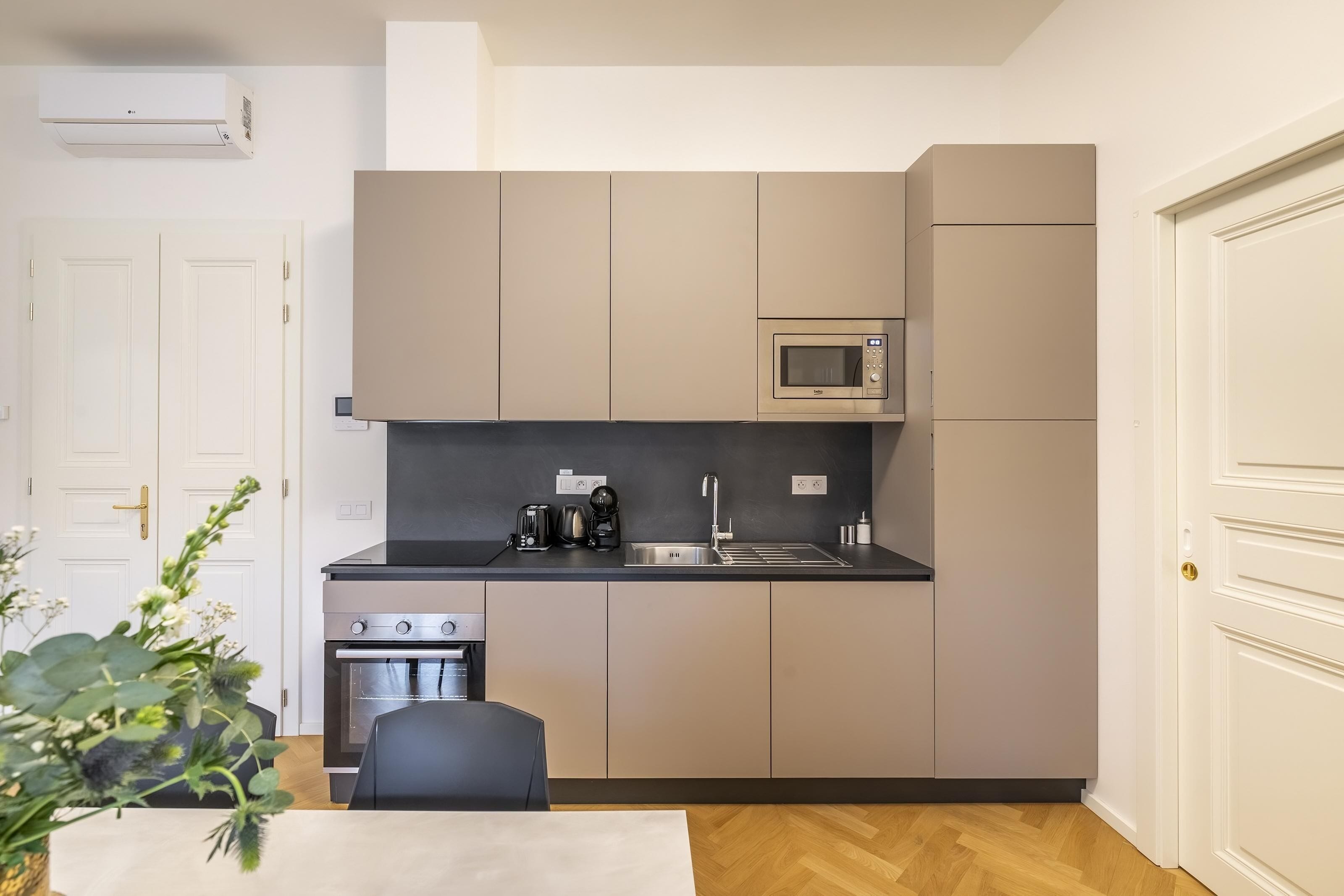Een kleine keuken met een magnetron, fornuis en spoelbak, een eethoekje en een deur met een handgreep.