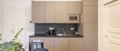 Een kleine keuken met een magnetron, fornuis en spoelbak, een eethoekje en een deur met een handgreep.