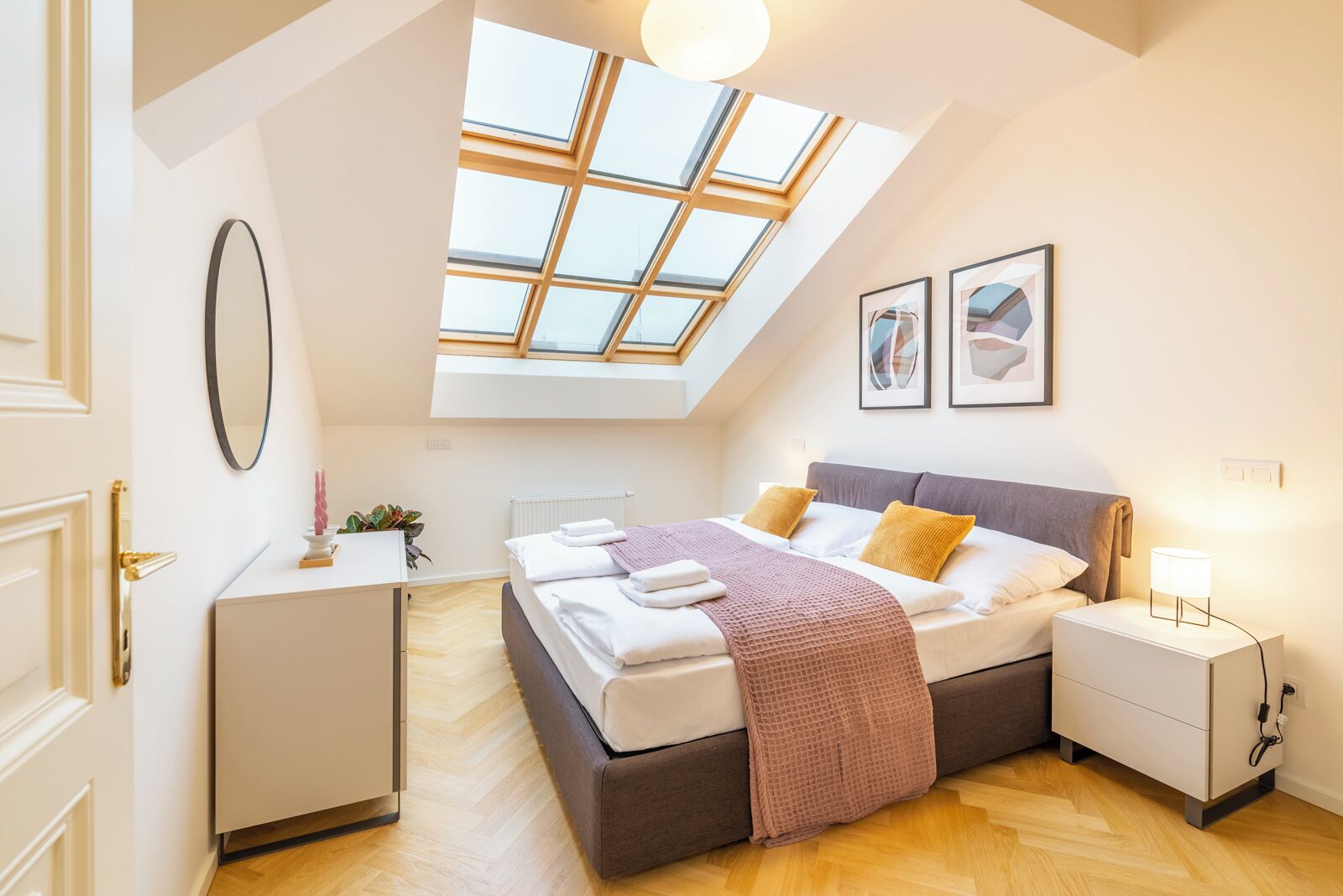 A bedroom with a skylight, a bed, bedside tables, a desk, and a mirror.