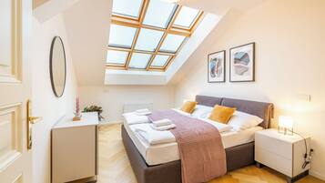 A bedroom with a skylight, a bed, bedside tables, a desk, and a mirror.