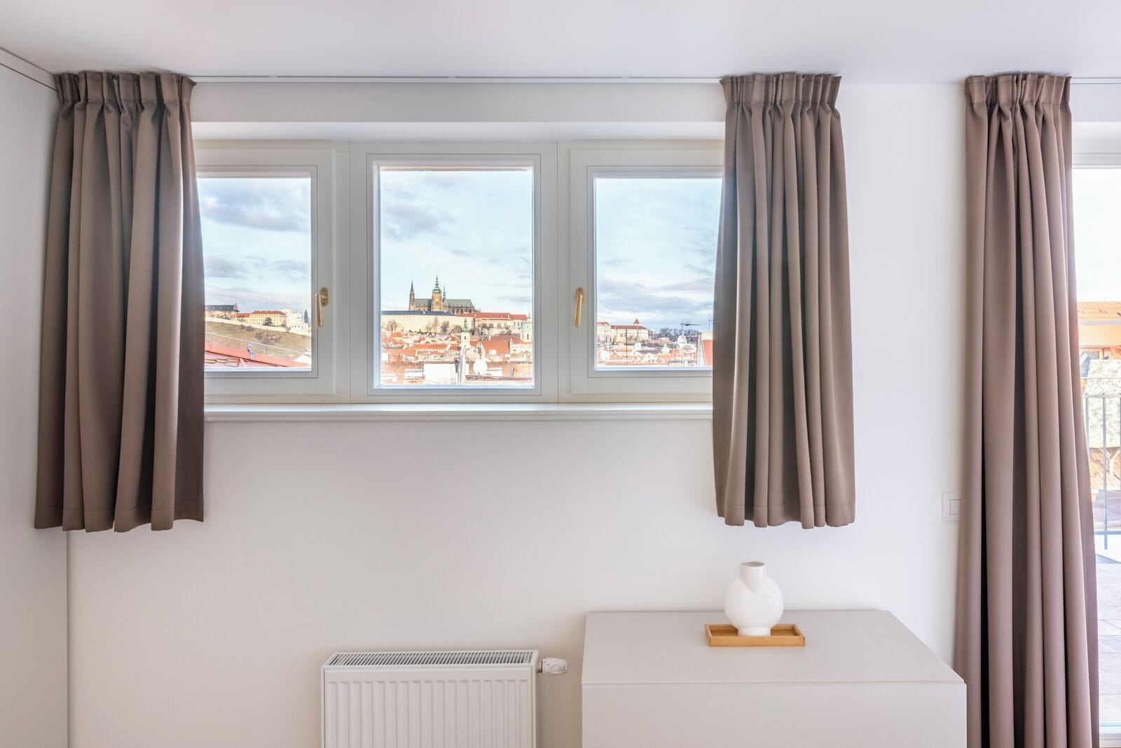 A room with three windows, each with curtains, and a radiator below.