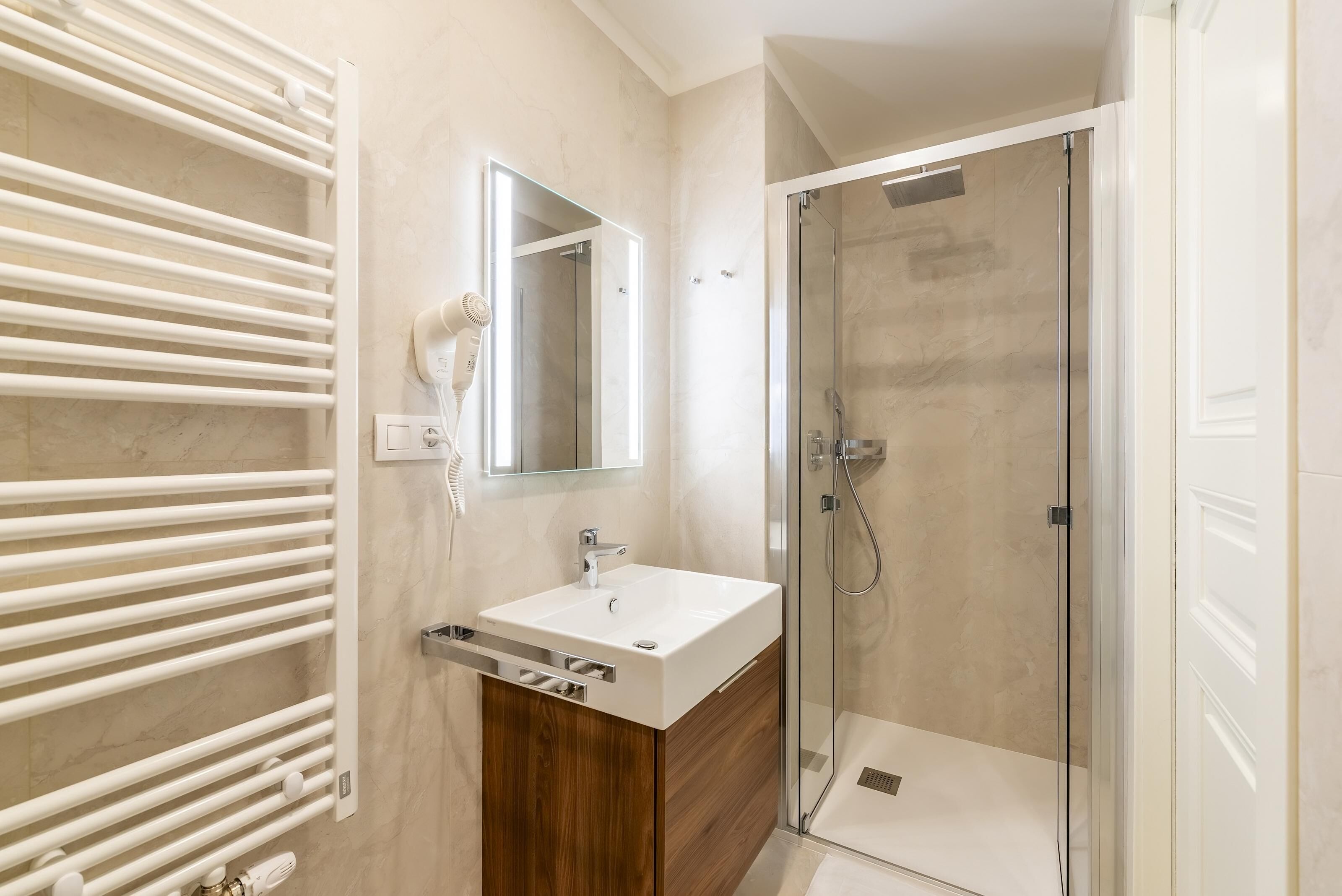 A modern bathroom with a white sink, wooden vanity, a glass shower enclosure, and a towel rack.