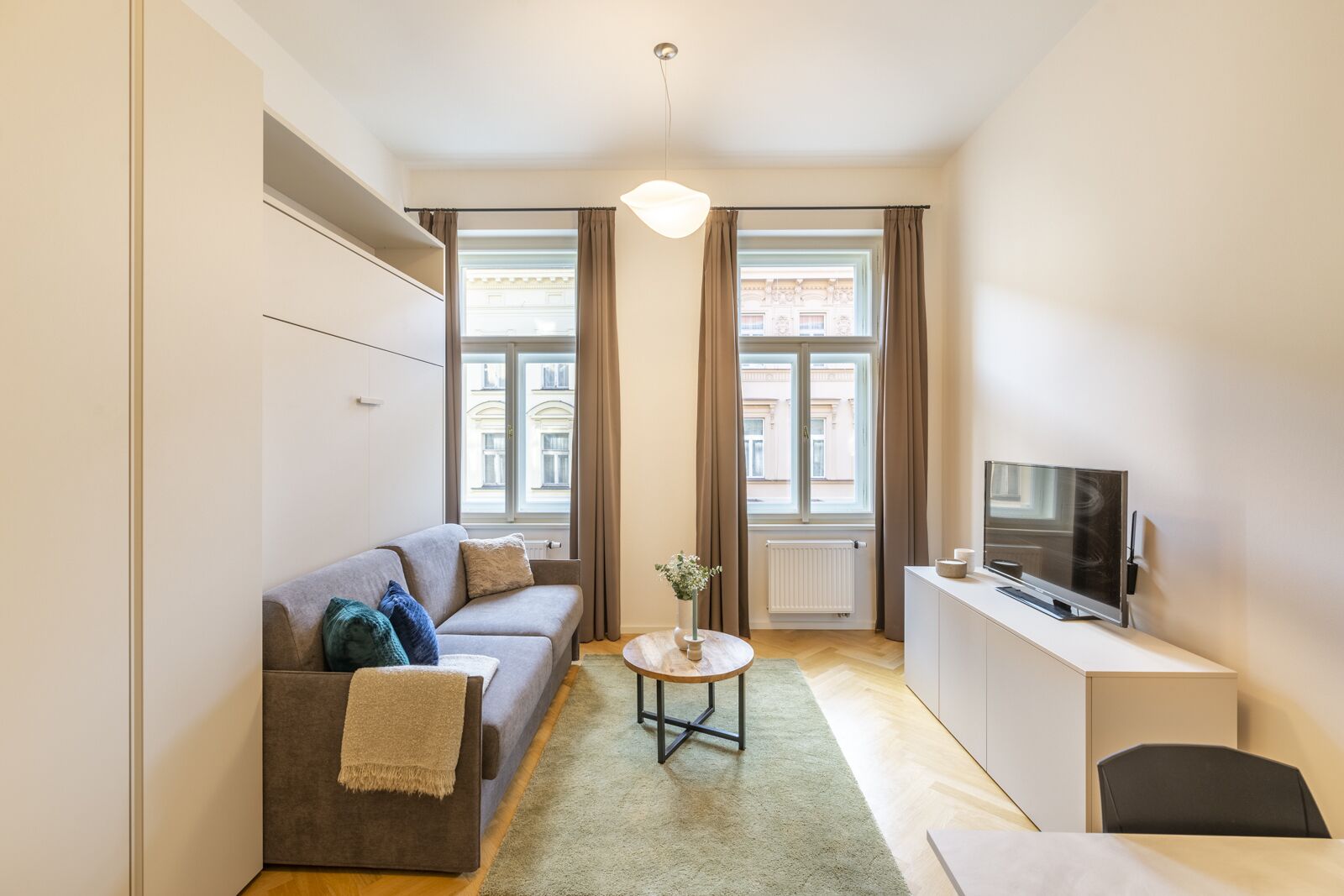 A modern living room with a sofa, a small table, a TV, and a window with curtains.