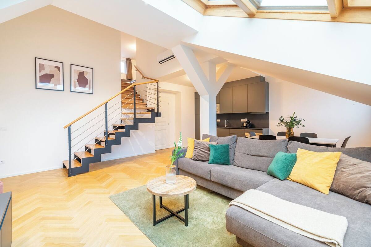 A spacious living area with a staircase, a sofa set, and a dining area.