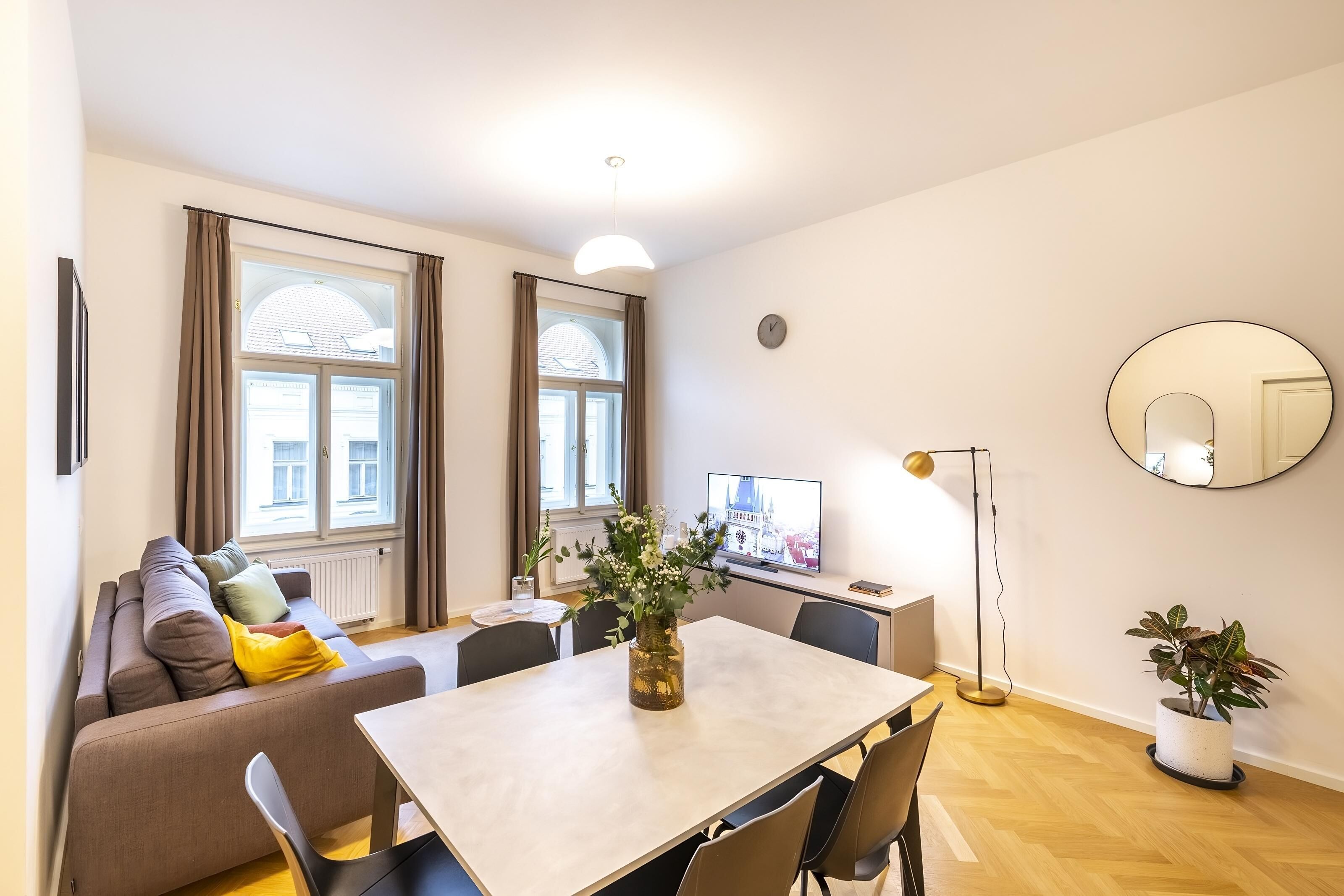 Una sala de estar moderna con un sofá, una mesa de comedor, sillas, un televisor, una lámpara de pie y dos macetas.