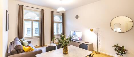Una sala de estar moderna con un sofá, una mesa de comedor, sillas, un televisor, una lámpara de pie y dos macetas.