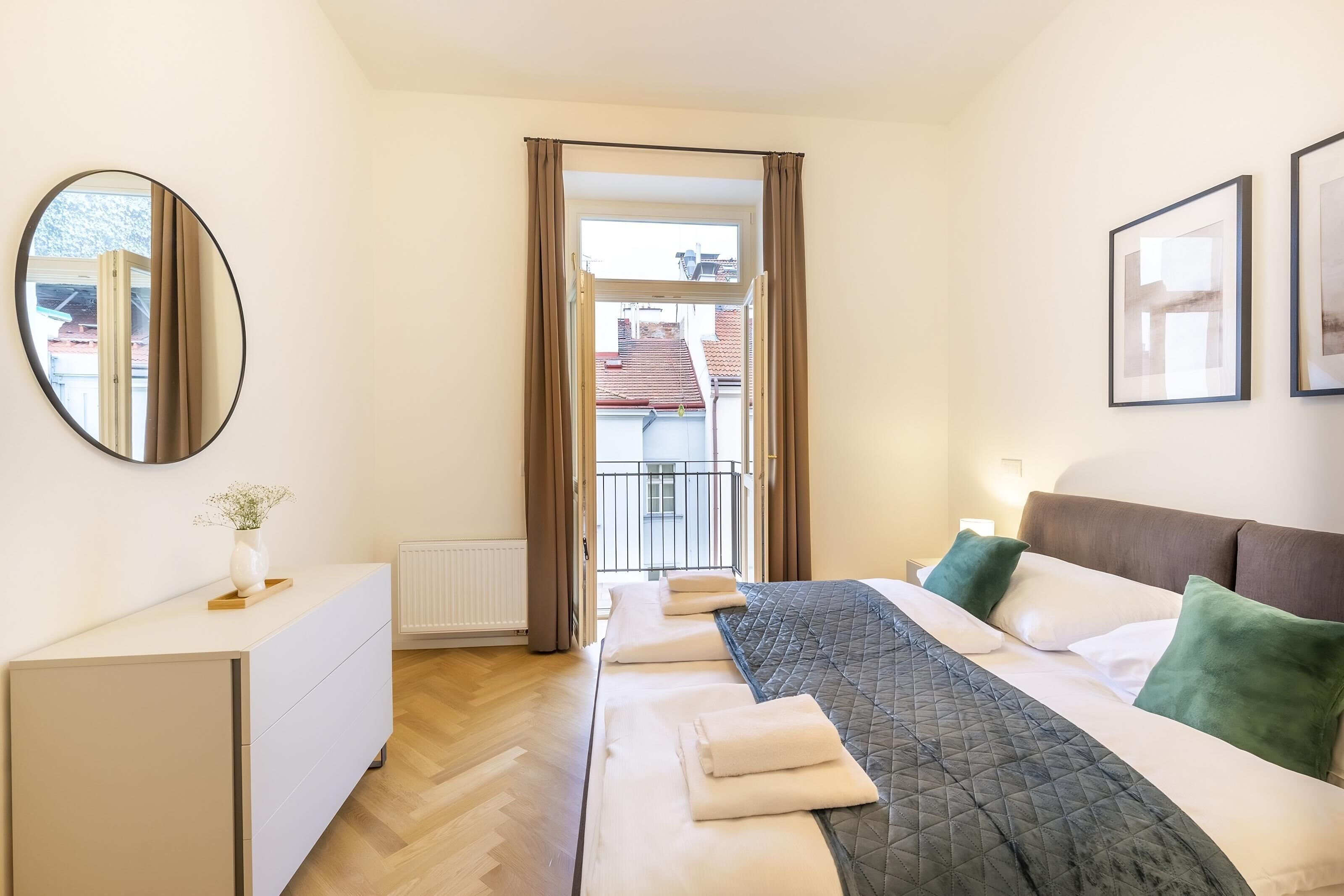 Ein Schlafzimmer mit Bett, Nachttischen, einem Schminktisch und einem Spiegel, mit Blick durch eine Tür.