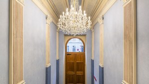 A grand hallway with a large wooden door, a chandelier, and classical architectural details. - Petrin Tower Residence (Prague)