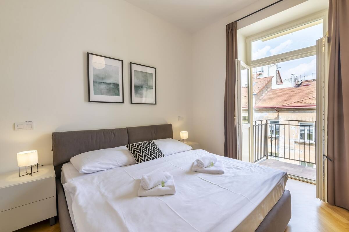 A neatly made bed with white linens and towels, a gray headboard, and two framed pictures on the wall.