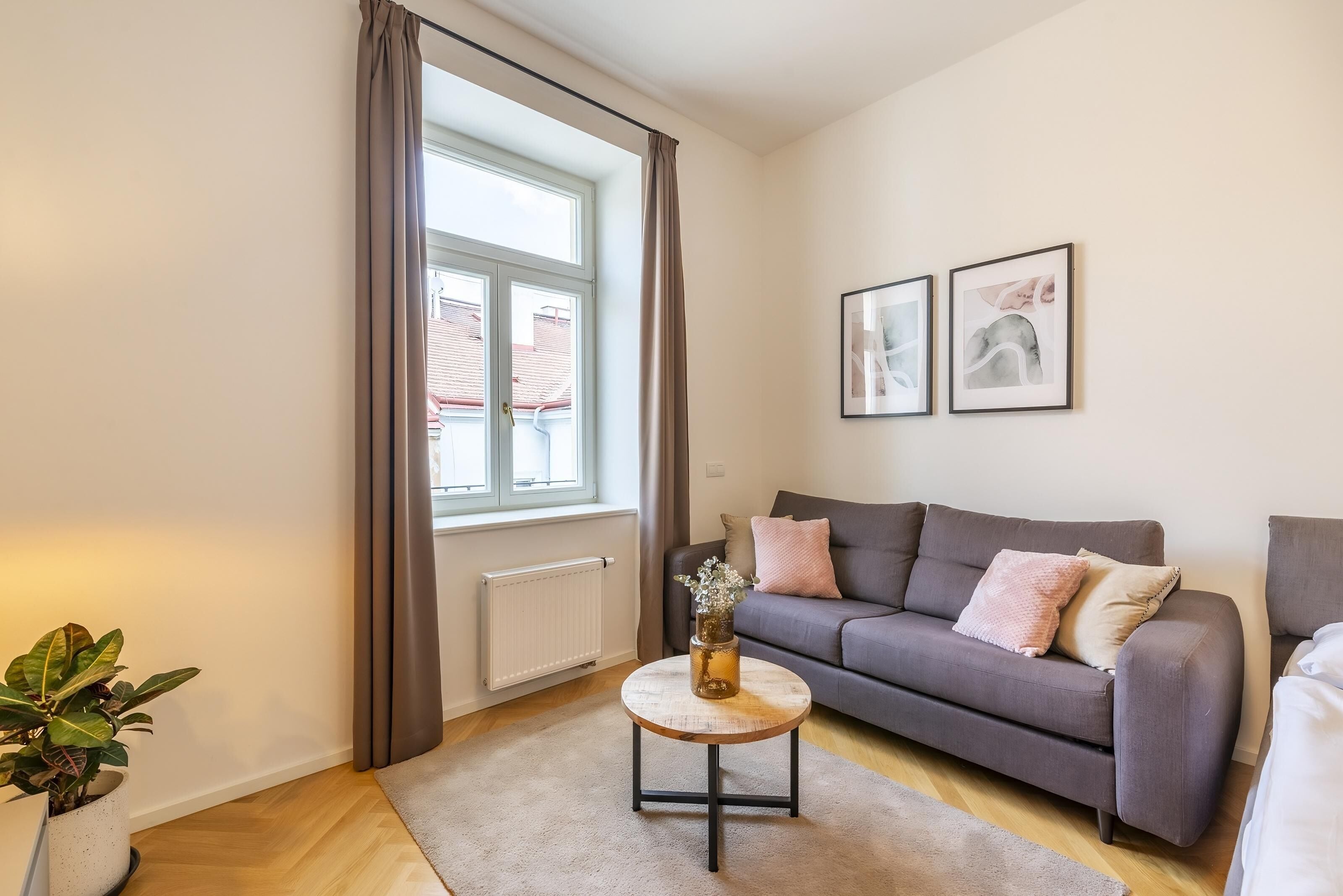 A modern living room with a grey sofa, a round coffee table, a potted plant, and a window with curtains.