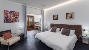Un dormitorio moderno con una cama grande, un sofá, una mesita y un cuadro en la pared.