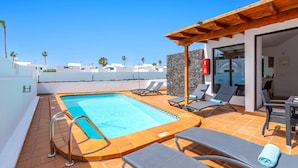 A rooftop pool area with lounge chairs and a stone wall. - Villa Famara by Villa Plus (Tías)