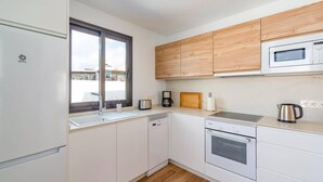 A modern kitchen with white cabinetry, a built-in oven, a microwave, and a coffee maker. - Villa Famara by Villa Plus (Tías)