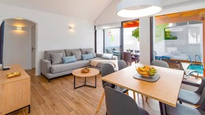 A modern living room with a grey sofa, a round coffee table, and a dining area with a wooden table and chairs. - Villa Famara by Villa Plus (Tías)