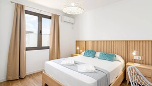 A modern hotel room with a wooden bed, a nightstand with a lamp, and a window with curtains. - Villa Famara by Villa Plus (Tías)