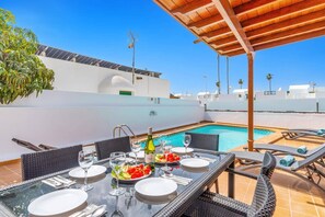 A rooftop dining area with a pool, outdoor seating, and a pergola.